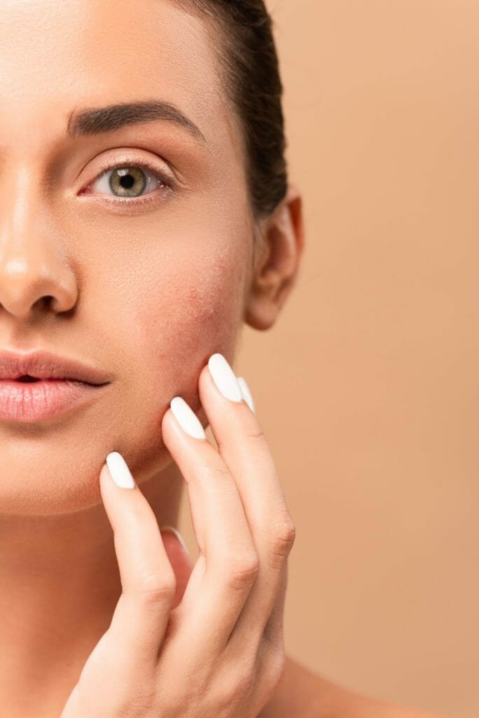 cropped view of girl touching clean face and looking at camera isolated on beige